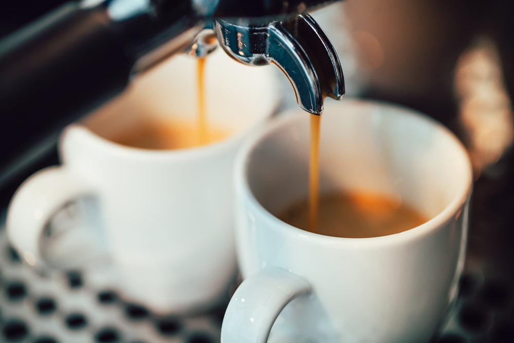Close up image of espresso pouring into two white cups.