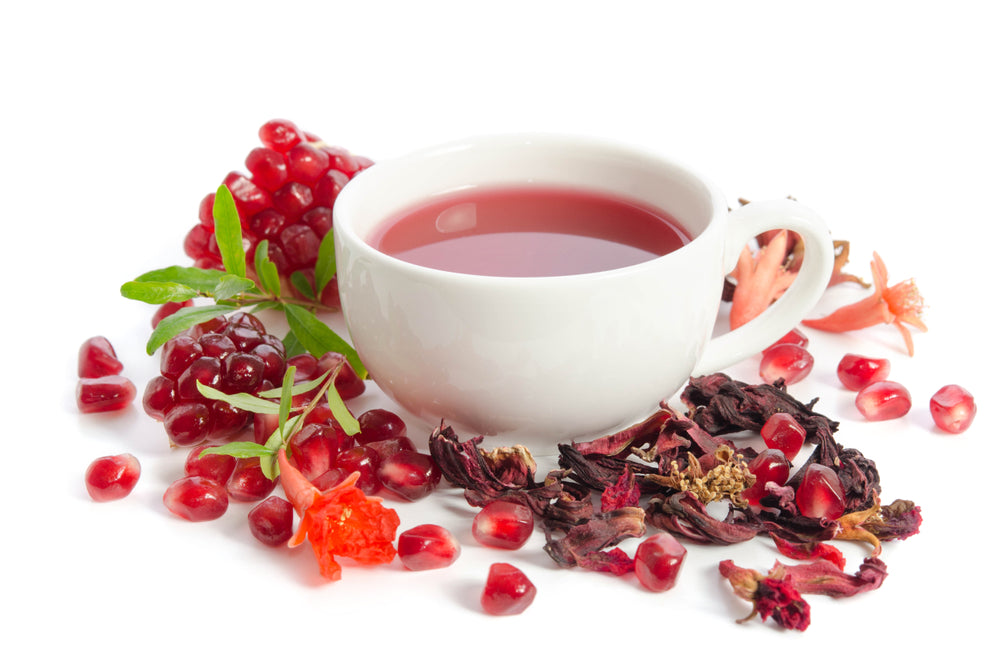 Cup of pomegranate green tea isolated on white background with parts of a pomegranate, seeds, leaves, flowers, and dry tea.