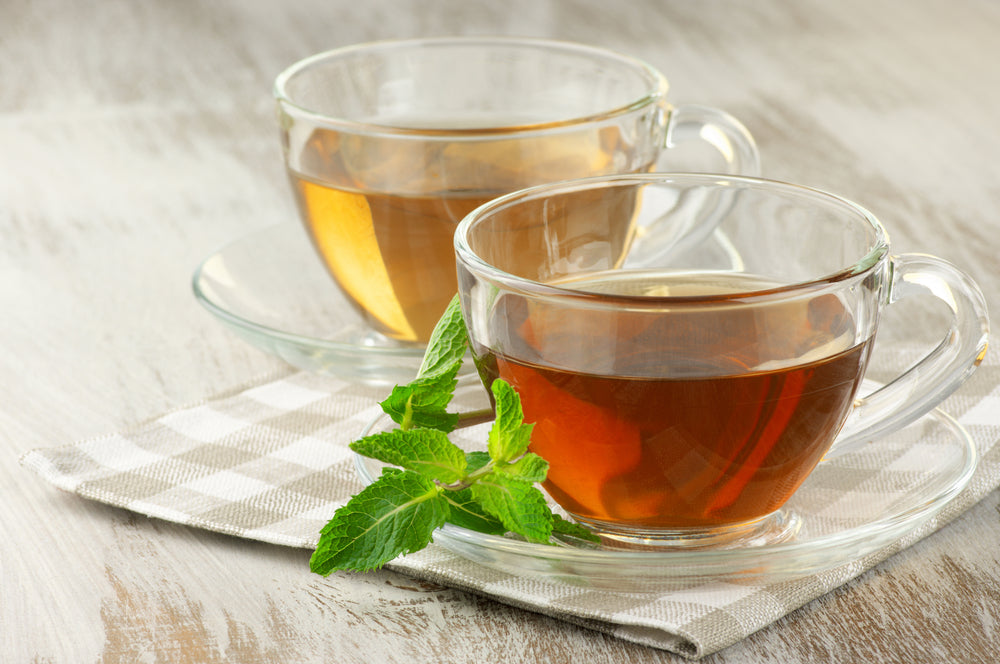 Cups of black and green tea with mint on rustic table.