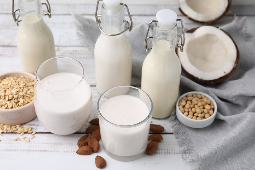 Different types of vegan milk alternatives and ingredients on white wooden table.