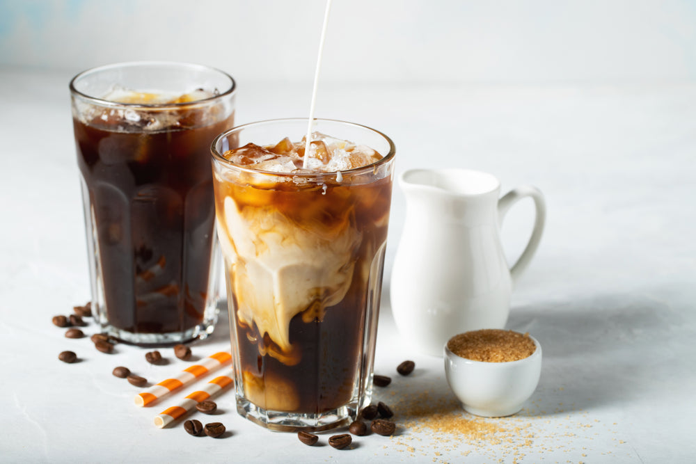 Iced Vietnamese coffee in a tall glass with cream poured over and coffee beans.