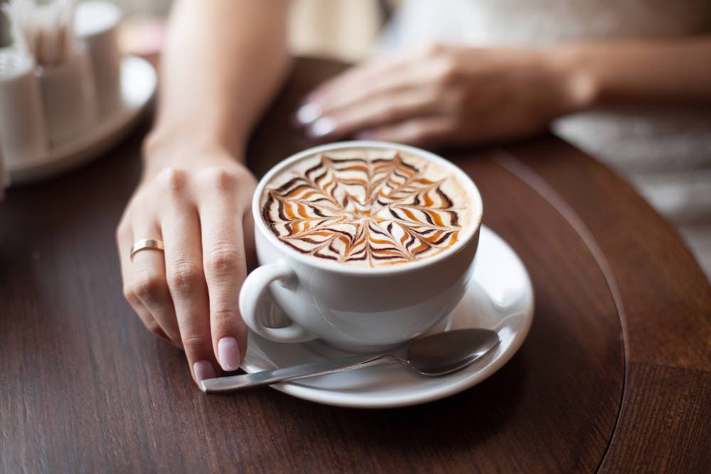 Latte Art coffee with a woman's right hand touching the saucer.