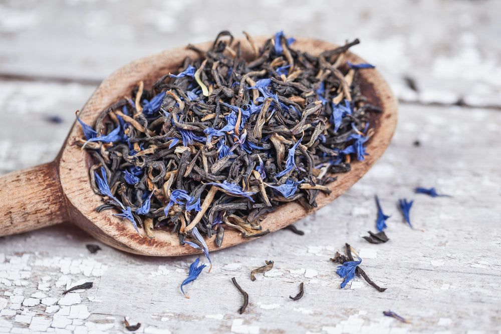 Loose Earl Grey tea leaves on a vintage wooden spoon and table.