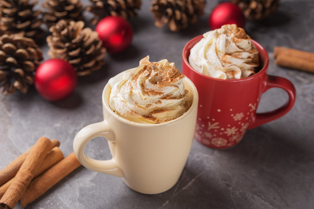 Pair of cups of hot chocolate or coffee with whipped cream on a dark table. Christmas and New Year's composition with red Christmas balls, pine cones, cinnamon sticks.