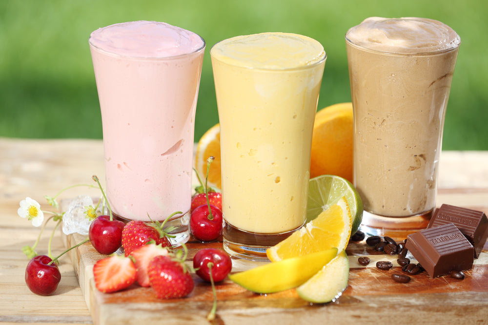 Three delicious smoothies with yogurt, two made with fruit and one of chocolate, together with various fresh tropical fruit on a garden table.