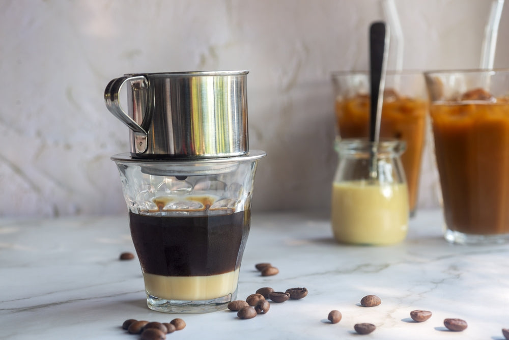 Vietnamese coffee with condensed milk in glass cups with traditional metal coffee maker phin on white table.