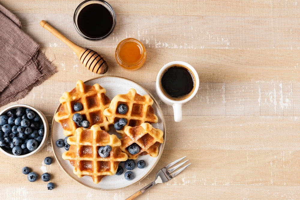 Waffles with blueberries, honey and cup of coffee on a wooden table.