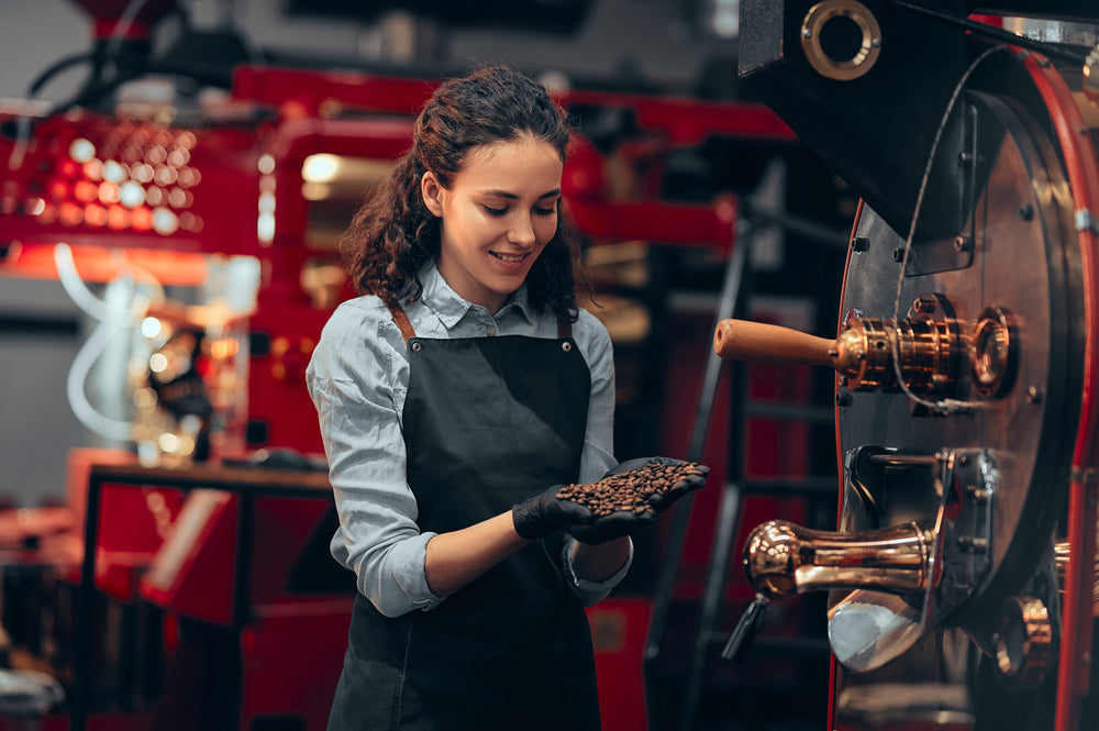 Woman checking the quality of the coffee beans standing near the roaster machine at the roastery.