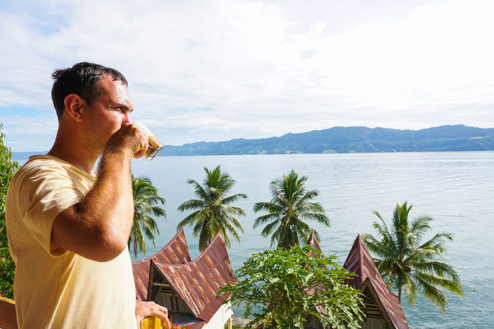 Young man drinking coffee and looking at Toba lake from Samosir island, North Sumatra, Indonesia.
