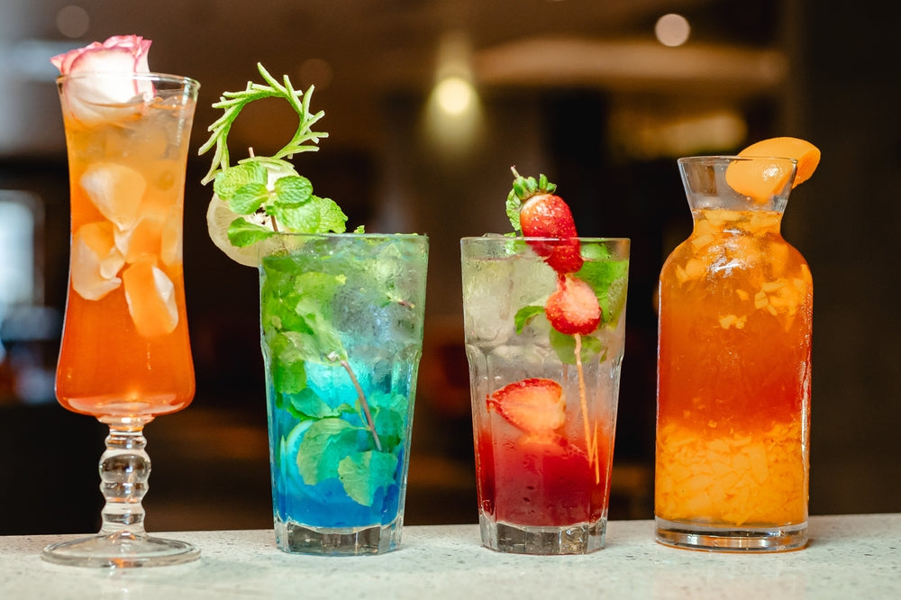 A vibrant lineup of four different colorful mocktails, garnished with fruits and mint.