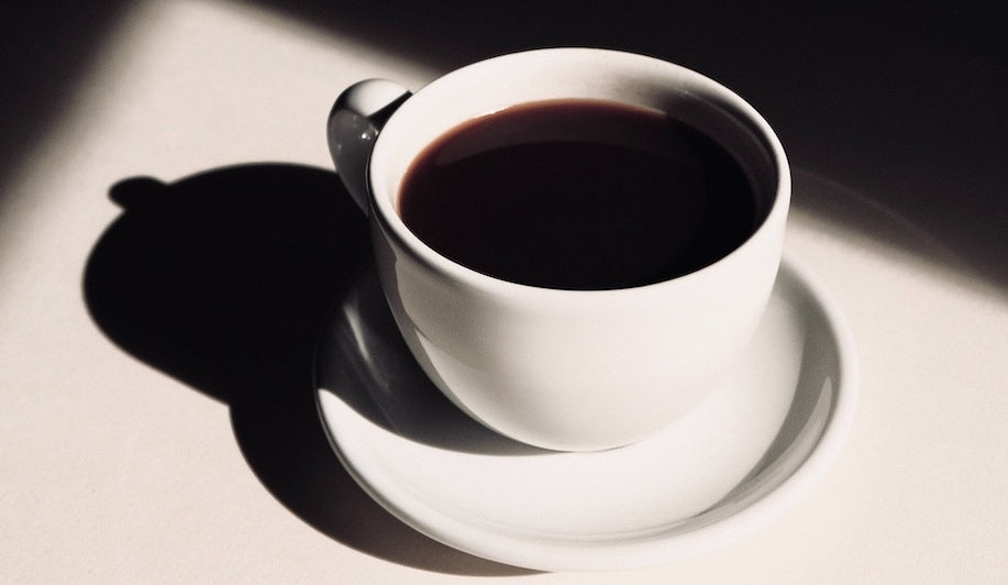 A white cup of black coffee and saucer on a white table.