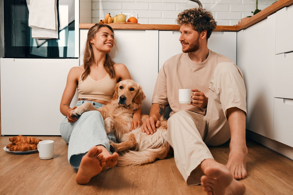A young married couple in love sitting on the floor in the kitchen drinking coffee in the morning with their beloved dog.