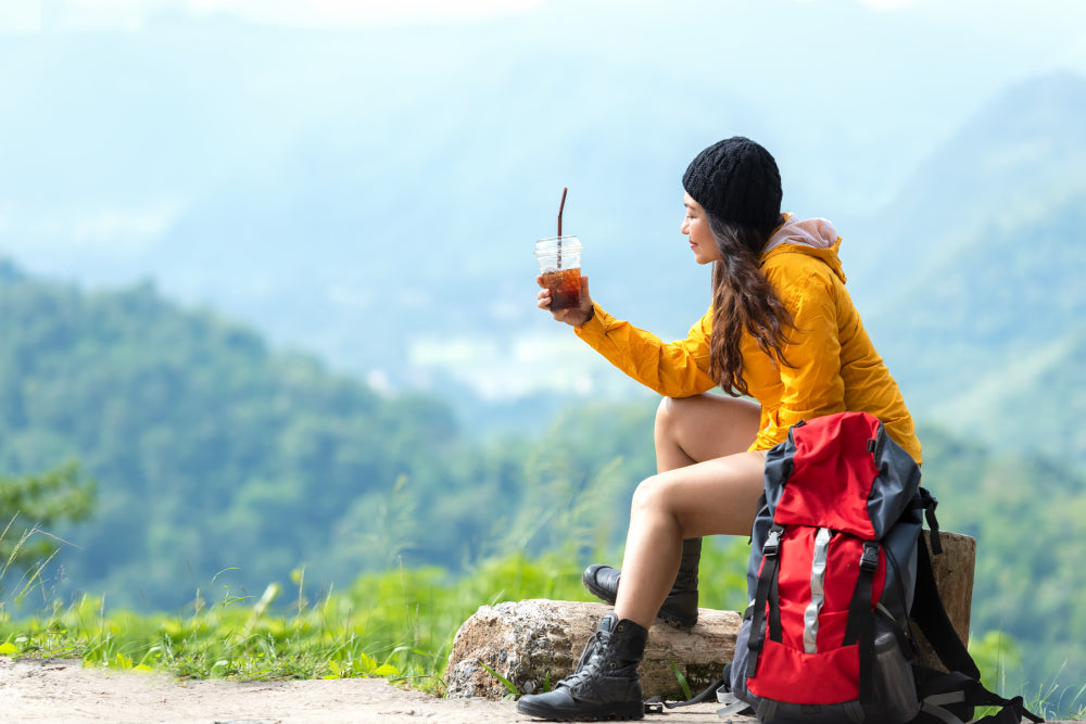 Asian women hiker with backpack sitting and drinking ice coffee and resting on the mountain.