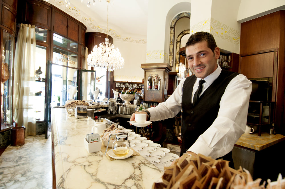Barista hands an espresso shot toward the camera at an espresso bar in Milan Italy.