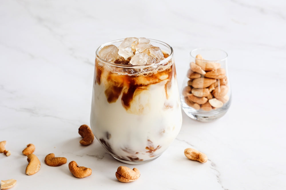 Close up homemade iced latte with plant base milk cashew nut milk with cashew nuts decorated on light background.