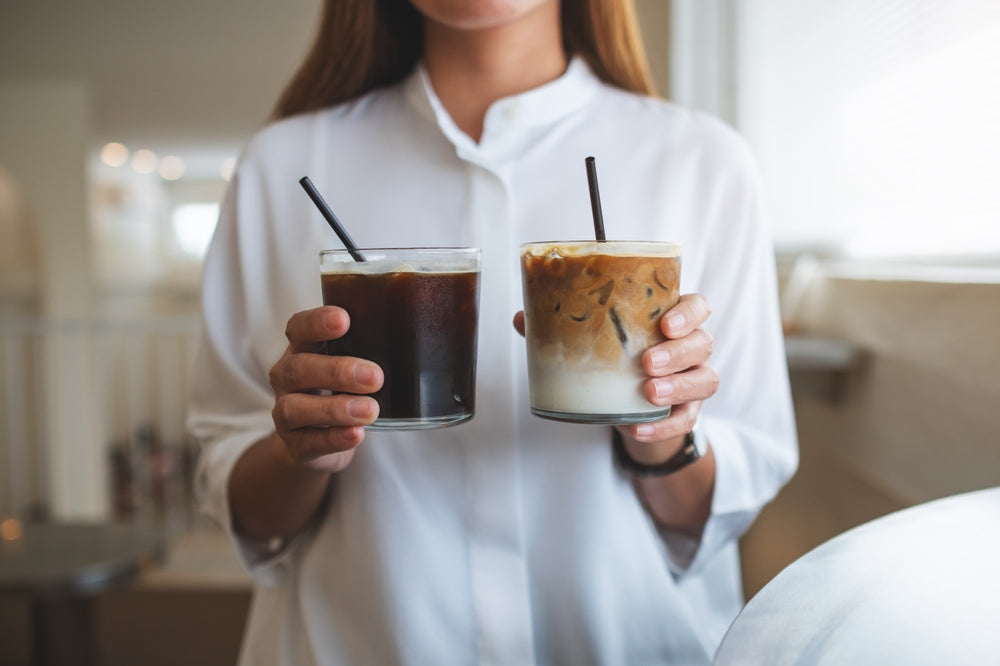 Closeup of a woman holding and serving two glasses of iced coffee.