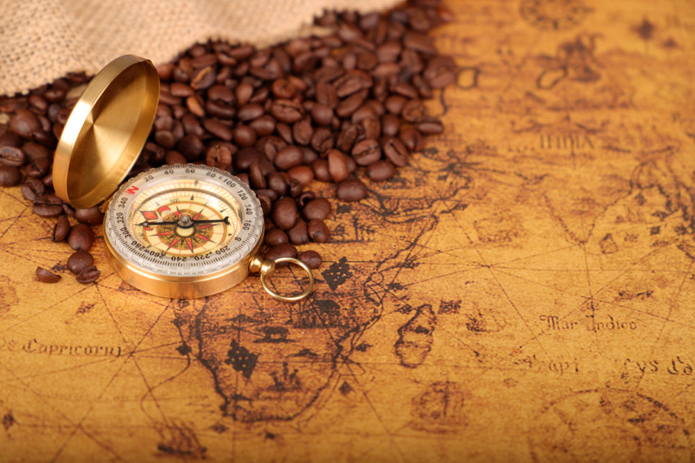 Coffee Beans and Vintage compass on an old world map with a trade and explorer concept.