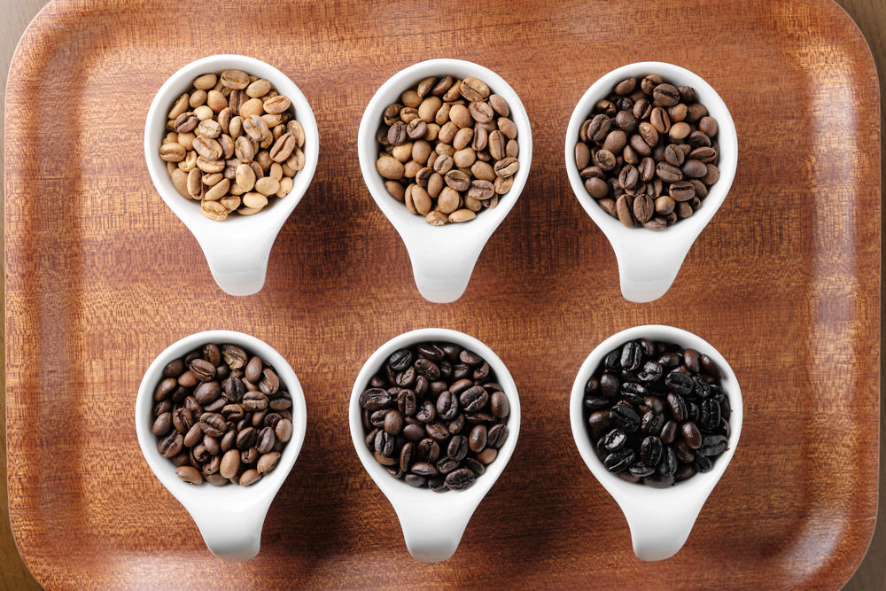 Coffee beans roasted in six stages in six white cups on a wooden tray.