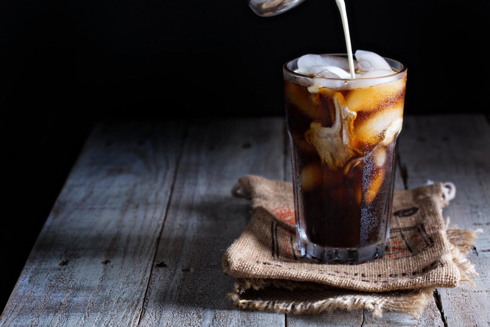 Cold brew coffee in a tall glass with milk pouring into the coffee.