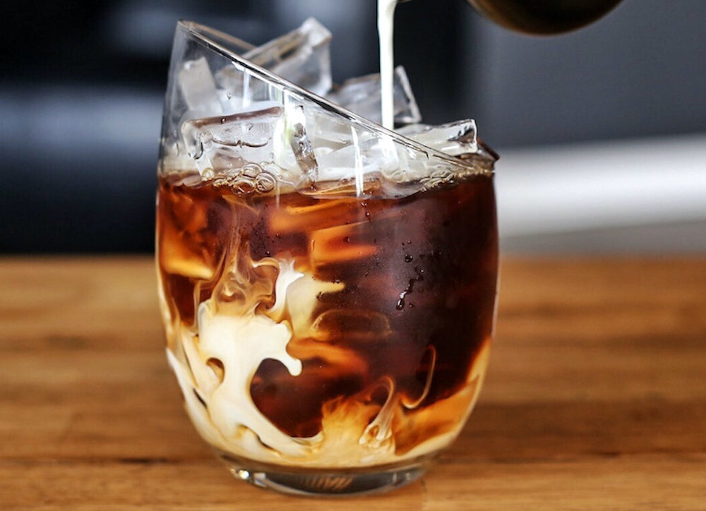 Cold brew coffee with milk pouring into an angled glass.