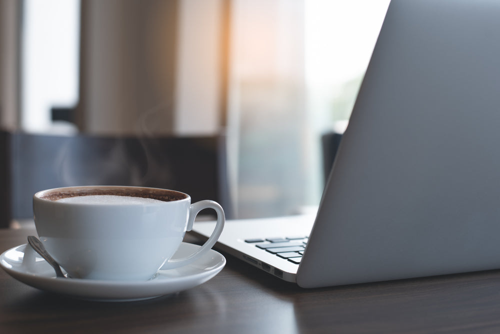 Cup of hot latte coffee and laptop computer on wooden table.