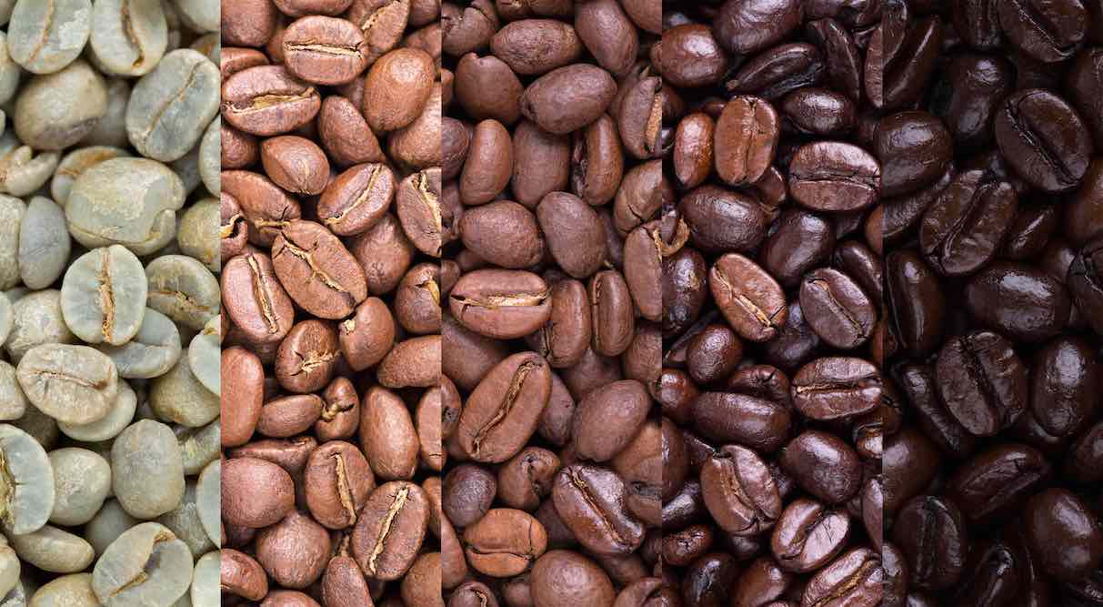 Four rows of coffee beans, green coffee beans, light roasted coffee beans, medium dark roasted coffee beans and dark roasted coffee beans.