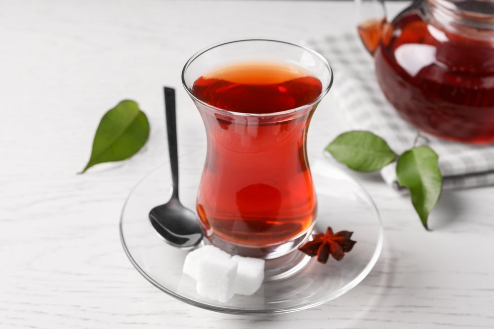Glass of traditional Turkish tea and sugar cubes on white wooden table.