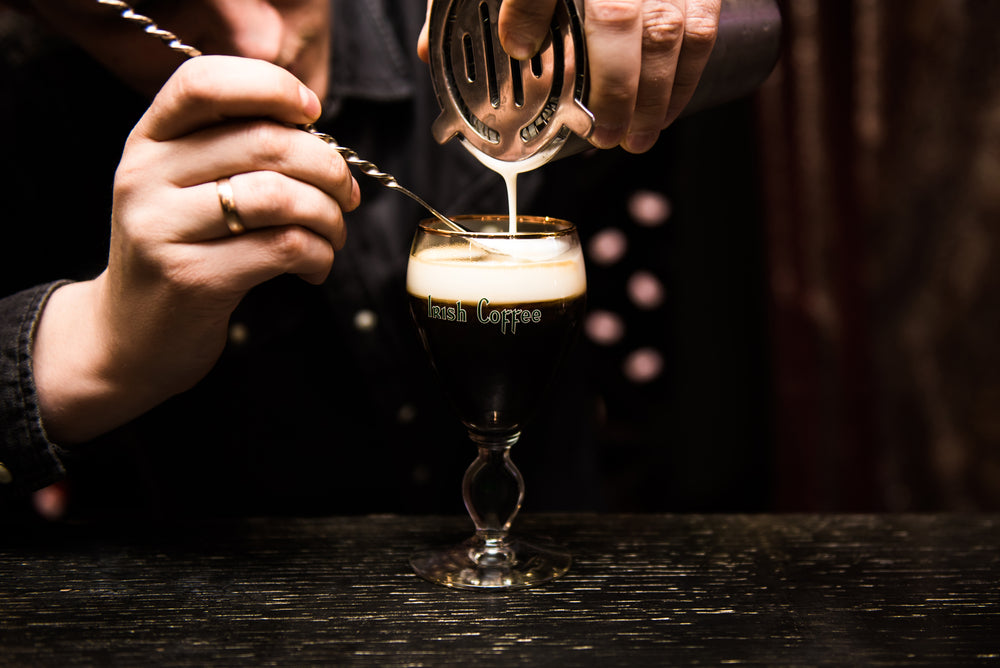 Irish Coffee cup with cream on a dark background on the bar.