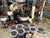 John Weaver Master Coffee Roaster leans over 45 kilo Probat Coffee roaster with fifty gallon buckets filled with roasted coffee beans in the foreground.