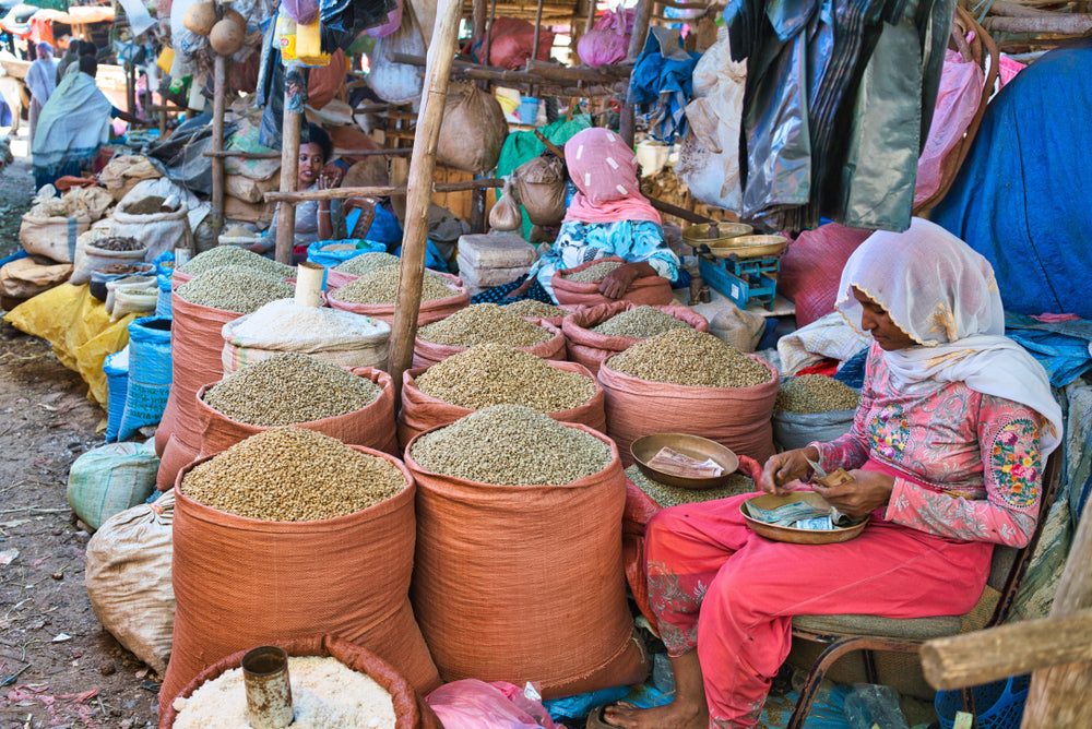Large burlap bags filled with coffee beans at the market in Ethiopia, while one woman is counting her money and other two women are talking.