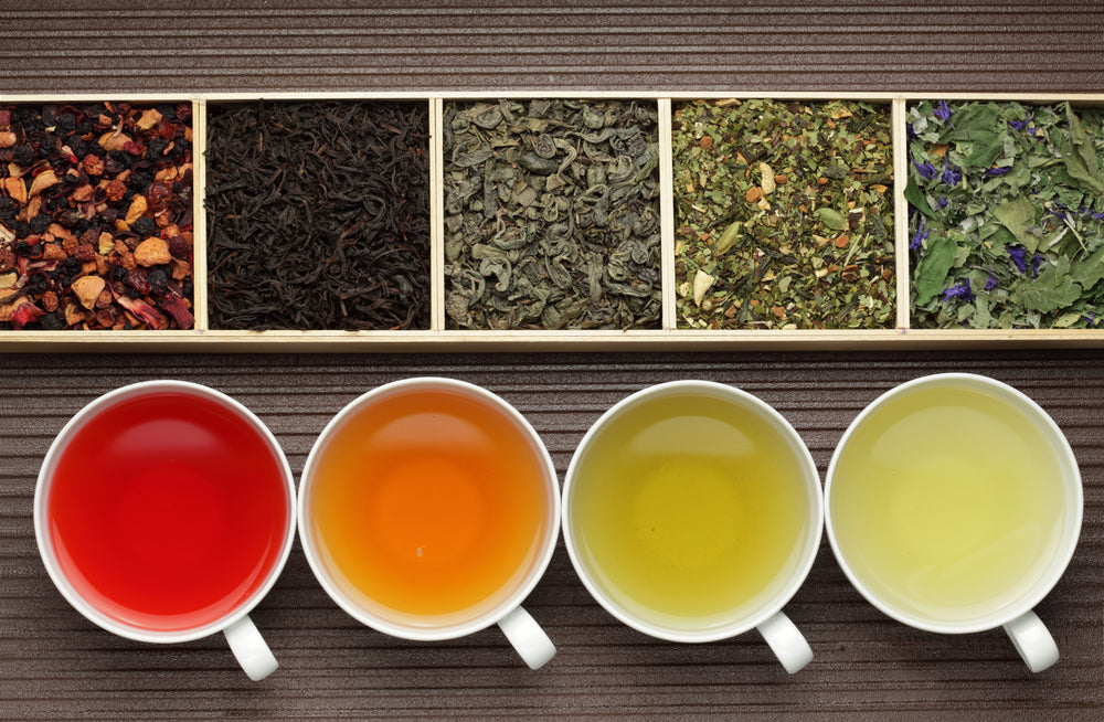 Loose leaf tea in boxes and white cups of brewed tea.