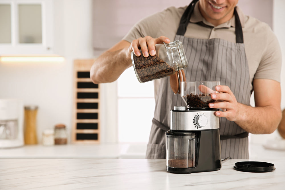 Man using electric coffee grinder in kitchen, closeup.