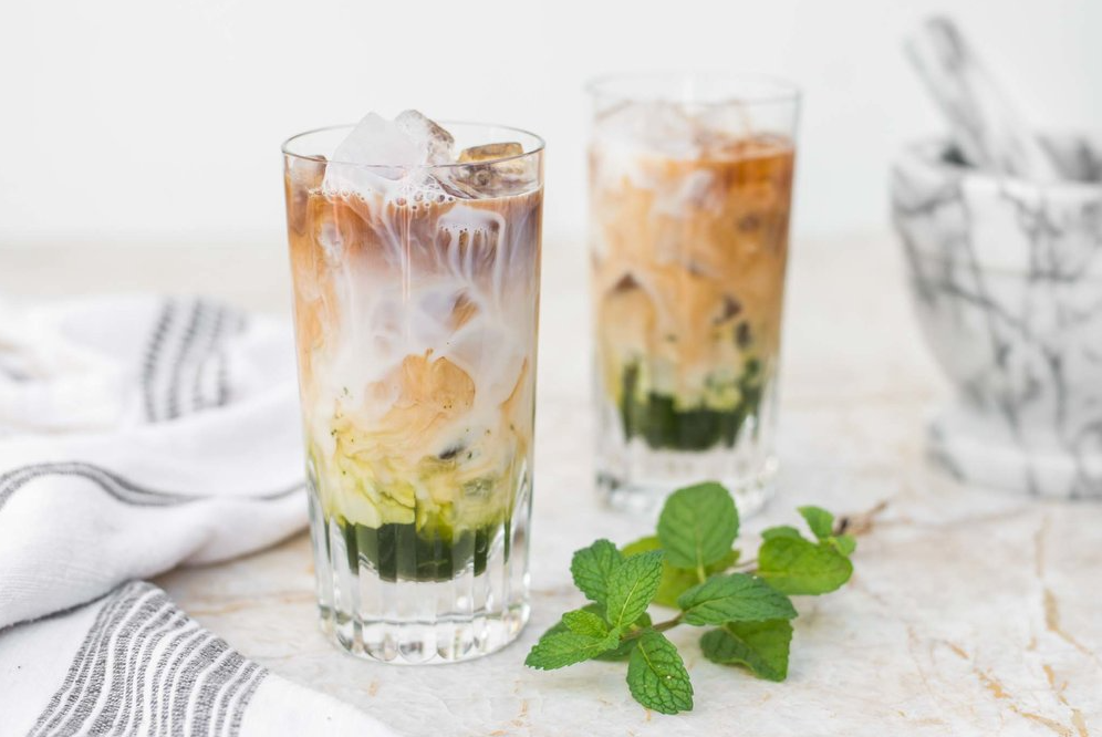 Two glasses of Mint Iced Latte with dishtowels in the background and mint leaves in the foreground.