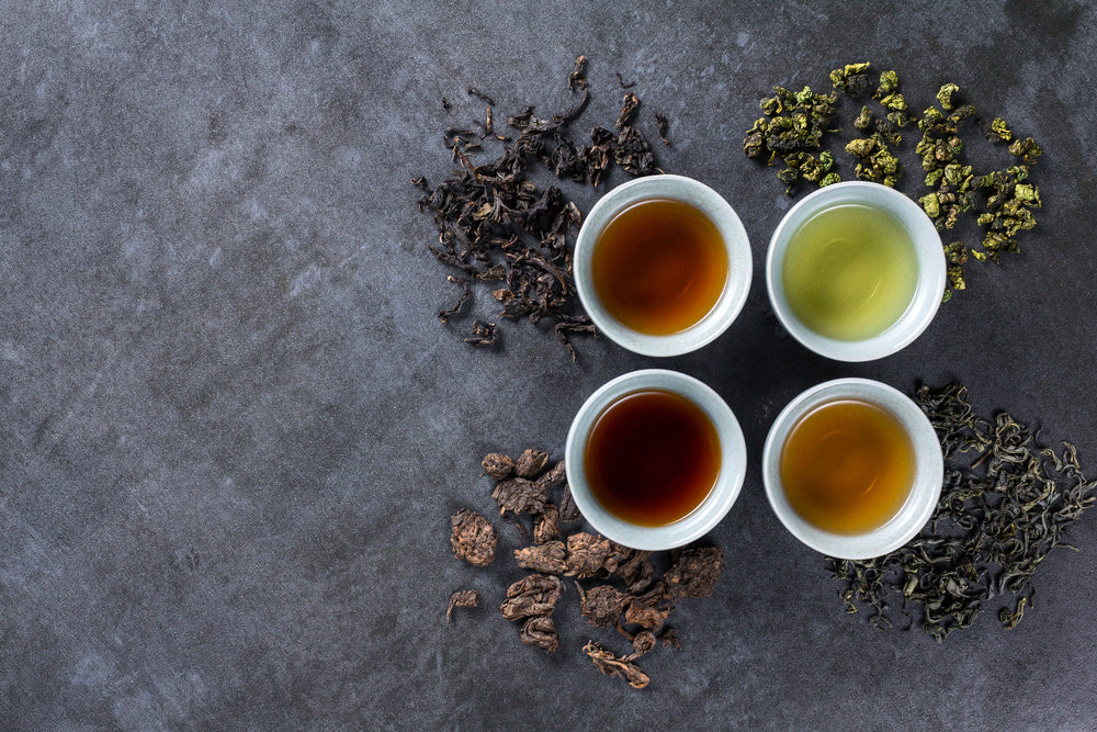 Oolong Tea brewed in four white tea cups with different types of loose leaf tea next to the cups.