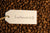 Text "Sustainability" written on a white paper tag on coffee beans.