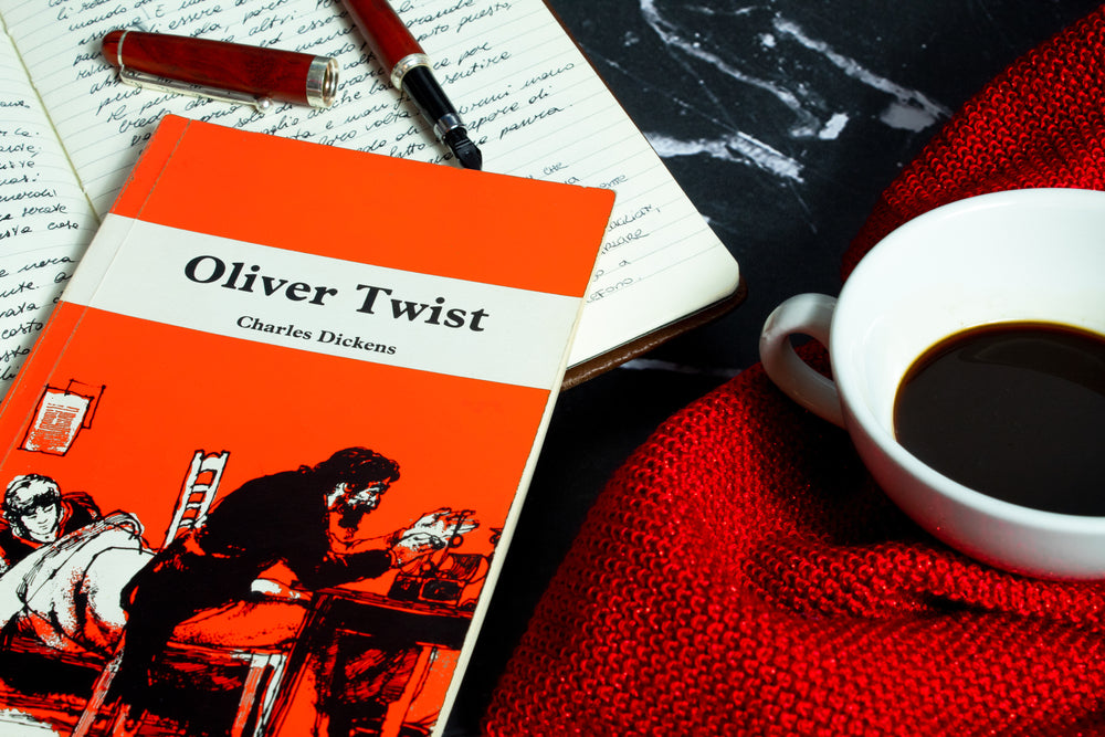 The book Oliver Twist by Charles Dickens next to a cup of coffee and a notebook with a fountain pen opened on it.