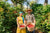 Two Guatemalan Coffee Farmers, women in yellow dress and man in large sun hat hold baskets of ripe coffee cherries.