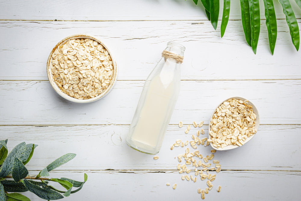 Vegan non dairy oatmeal milk in bottles on white wooden background.