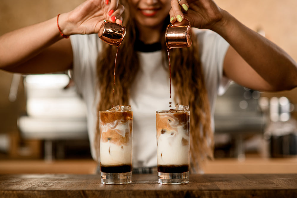 Woman carefully pours espresso from cups into glasses with ice, milk and syrup