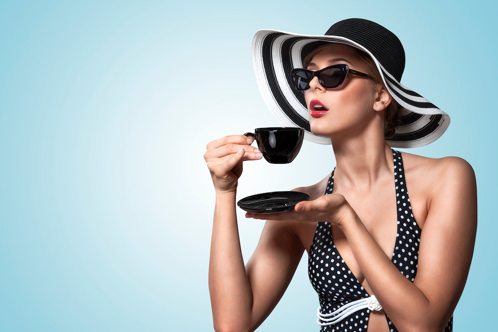 Woman in a Black and White striped sun hat drinking coffee from a black coffee cup.