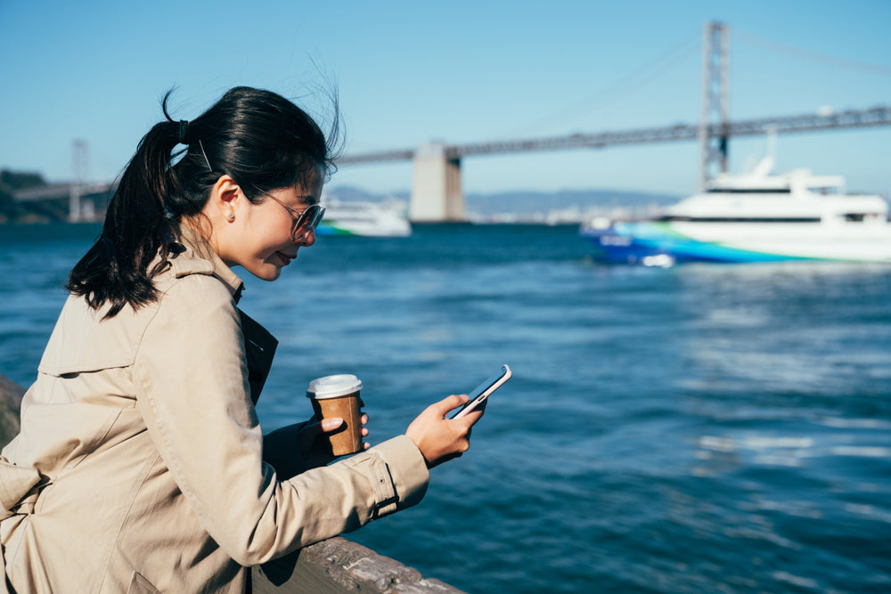 Woman using phone with San Francisco Oakland Bay Bridge and Treasure Island aerial in background.