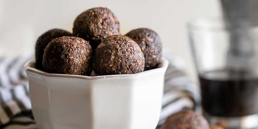 Five energy bites balls in a white ceramic bowl.